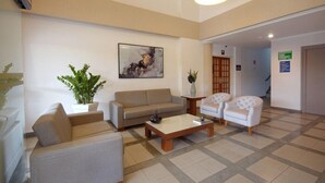 Un amplio vestíbulo con un sofá color crema, un sillón blanco, una mesa de centro y una planta en maceta.