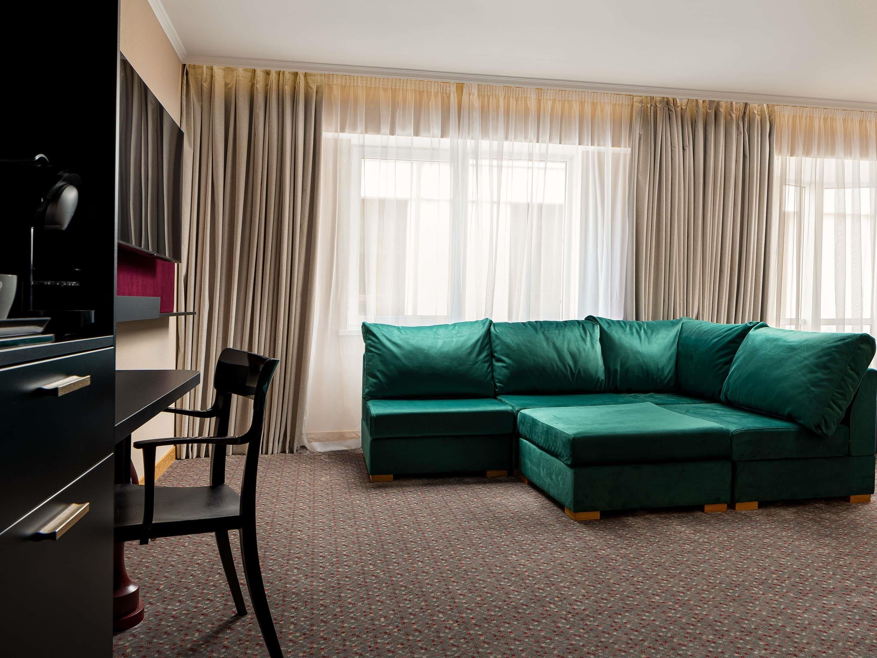 Ein Zimmer mit einem grünen Ecksofa, einem Schreibtisch mit Stuhl und einem Fernseher.