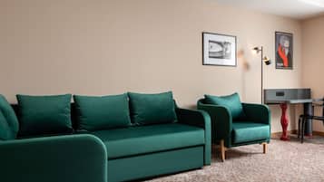 A room with a green sofa set, a small table with a red base, and two framed pictures on the wall.
