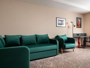 Een kamer met een groene zithoek, een klein tafeltje met rood onderstel en twee ingelijste foto's aan de muur.