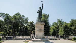 A statue of a figure holding a cross on a pedestal in a park with trees and a fence in the background. - Mercure Chisinau Center Jazz Hotel (Chisinau)