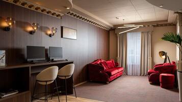 A modern hotel room with a wooden desk, two monitors, a red sofa, and a red armchair.