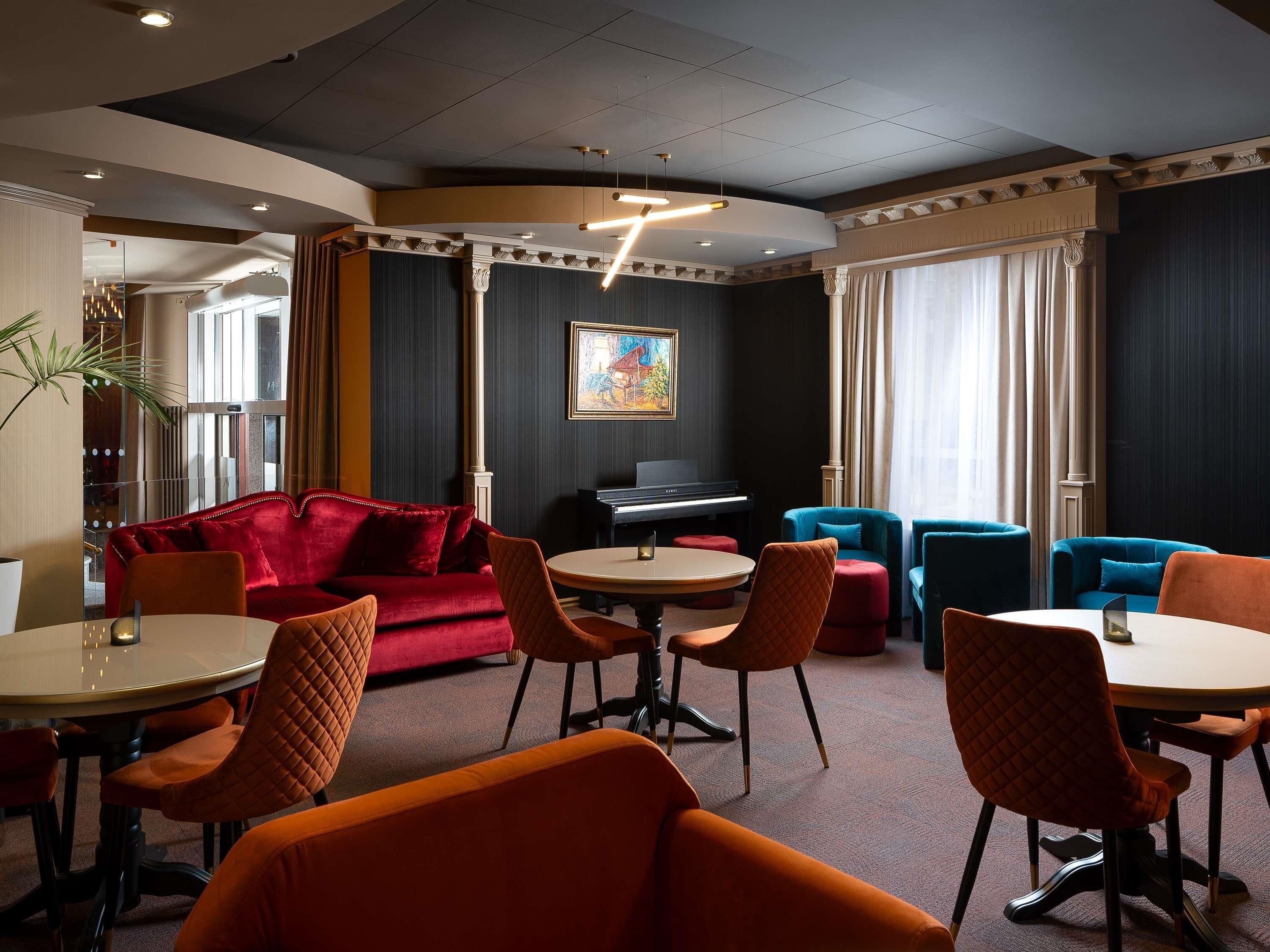 A modern lounge area with a red sofa, blue armchairs, and orange chairs around a central table.