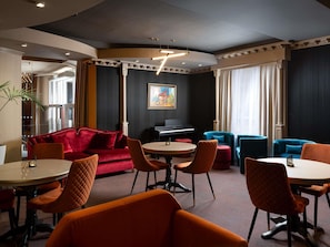 A modern lounge area with a red sofa, blue armchairs, and orange chairs around a central table.