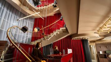 A grand staircase with red curtains, a piano, and a reception desk in a luxurious lobby.