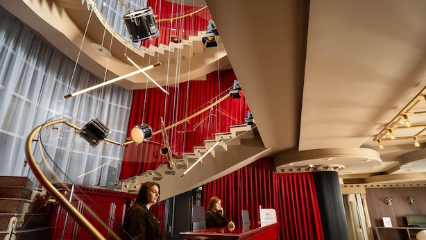 En imponerende trappe med røde gardiner, et klaver og en receptionsdisk i en luksuriøs lobby.