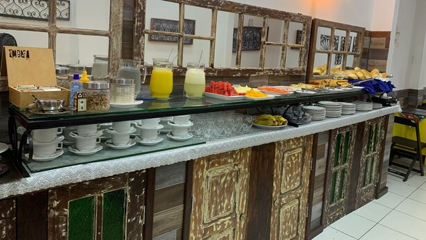 A buffet setup with various food items, a coffee station, and a decorative wall with a rustic design. - Pousada Suites do Pelo (Salvador)