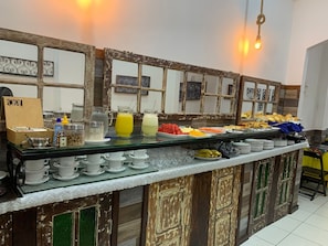 Montaje de bufé con diversas opciones de comida, una estación de café y una pared decorativa con diseño rústico.