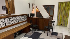 A reception area with a wooden bench, two chairs, a desk, a computer, and a cross on the wall. - Pousada Suites do Pelo (Salvador)