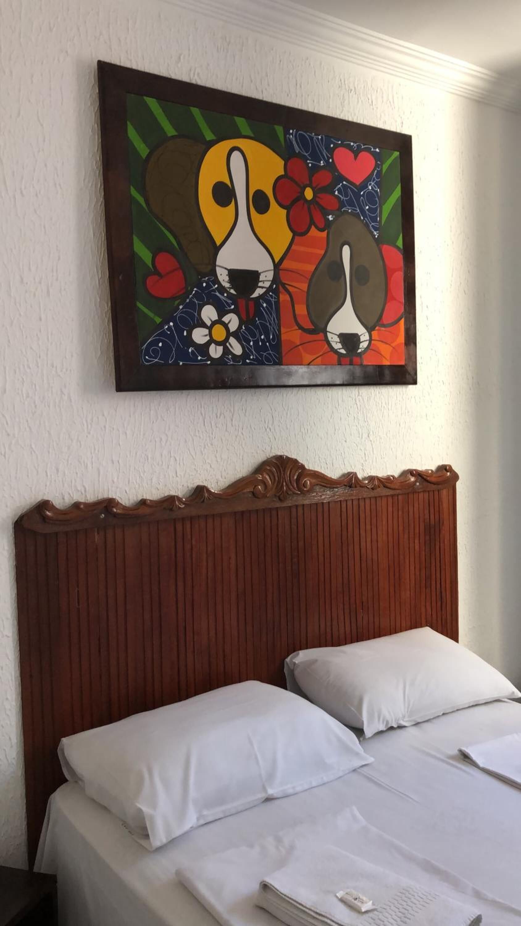 Habitación de hotel con cabecera de madera, cama con ropa blanca y un cuadro colorido sobre la cama.
