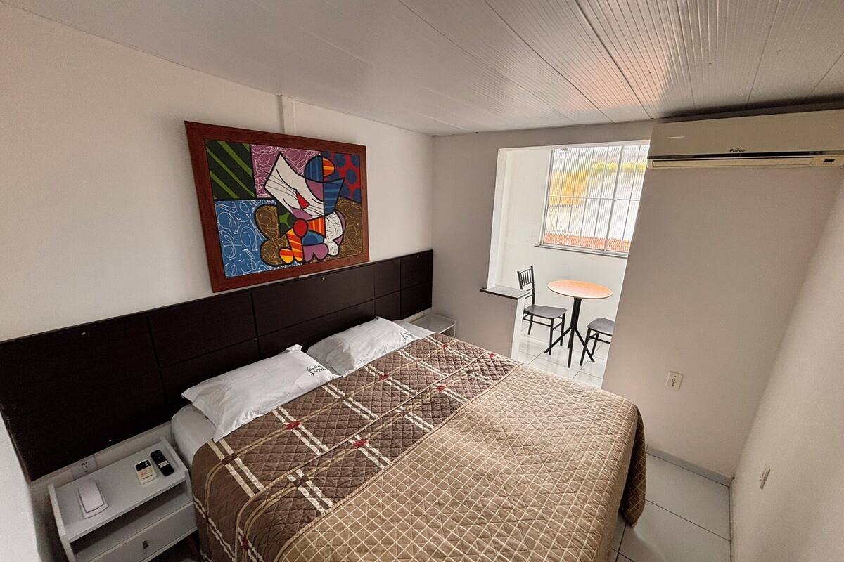 Een slaapkamer met een bed, nachtkastje, stoel, klein tafeltje en raam.