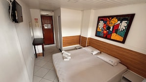A hotel room with a bed, a desk, a chair, a television, and a painting on the wall. - Pousada Suites do Pelo (Salvador)