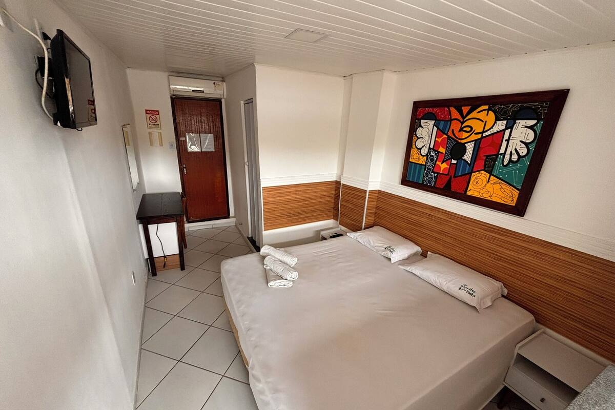 Een hotelkamer met een bed, een bureau, een stoel, een televisie en een schilderij aan de muur.