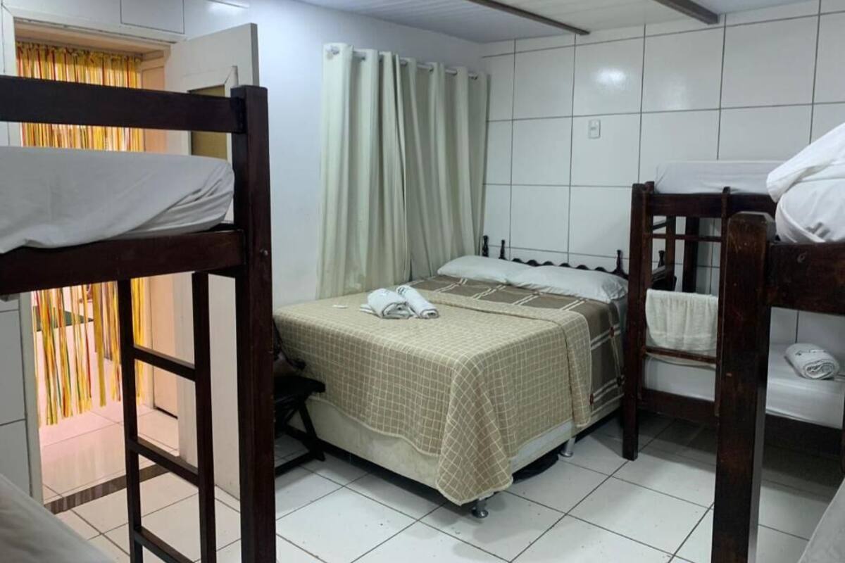 Een kamer met stapelbedden, een enkel bed, een gordijn en een betegelde vloer.