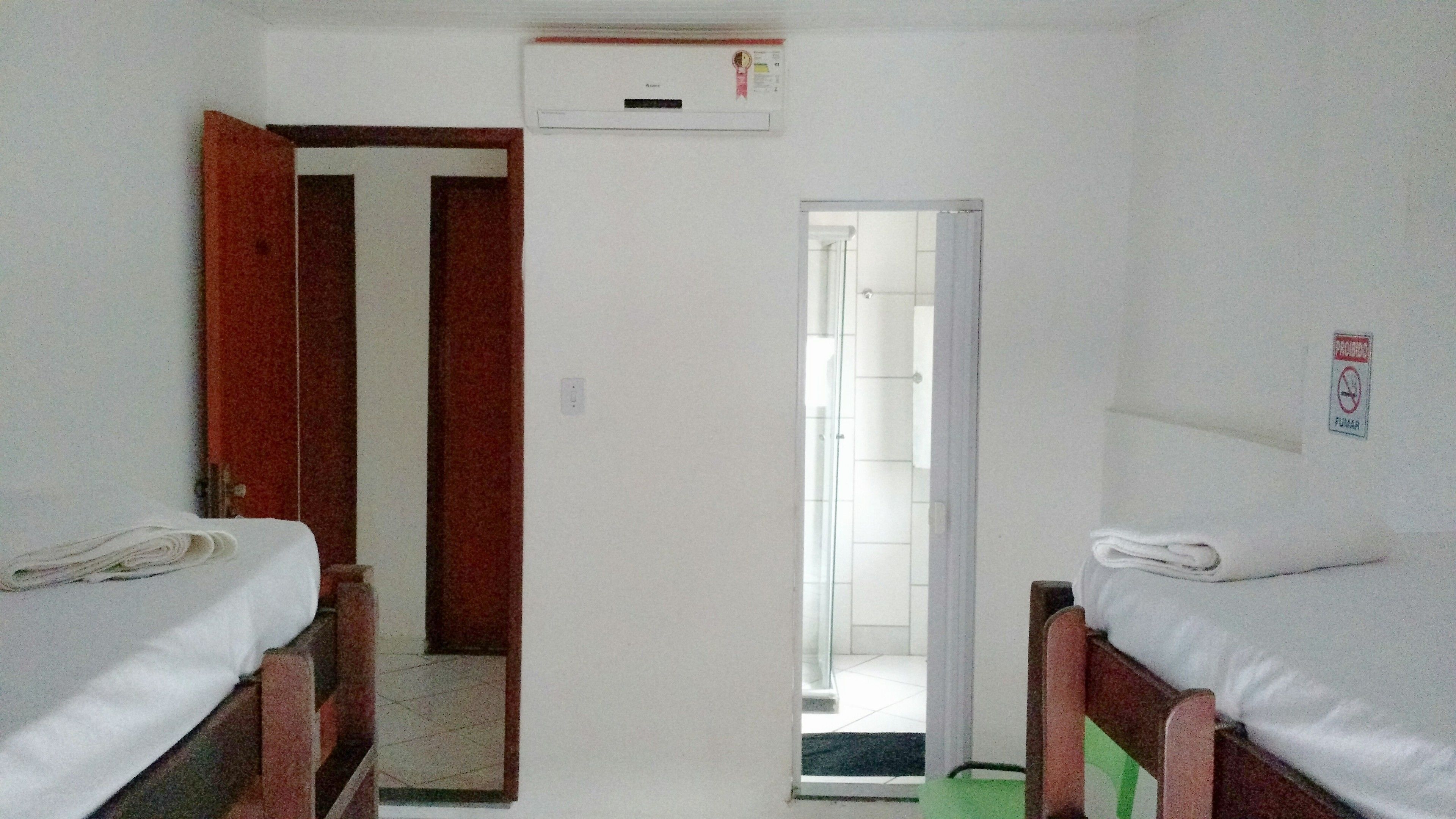 Una habitación pequeña y poco amueblada con dos camas individuales, una puerta que da al baño y un aire acondicionado instalado en la pared.