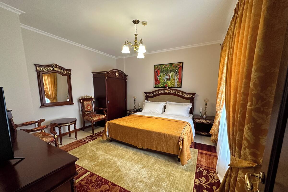 Een hotelkamer met een groot bed, een bureau, een stoel, een kledingkast en een schilderij aan de muur.