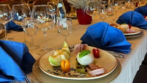 Une table à manger dressée avec des assiettes, des verres et des couverts, agrémentée d’un centre de table décoratif et surmontée d’un plafond en bois chaleureux.