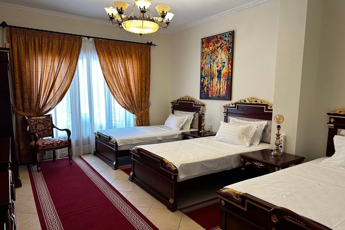 Een hotelkamer met twee houten bedden, een rood tapijt, een kroonluchter en een schilderij aan de muur.