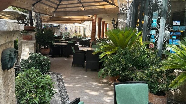 Un espace café en plein air, avec des tables et des chaises, entouré de plantes en pot et doté d’un coin salon abrité.