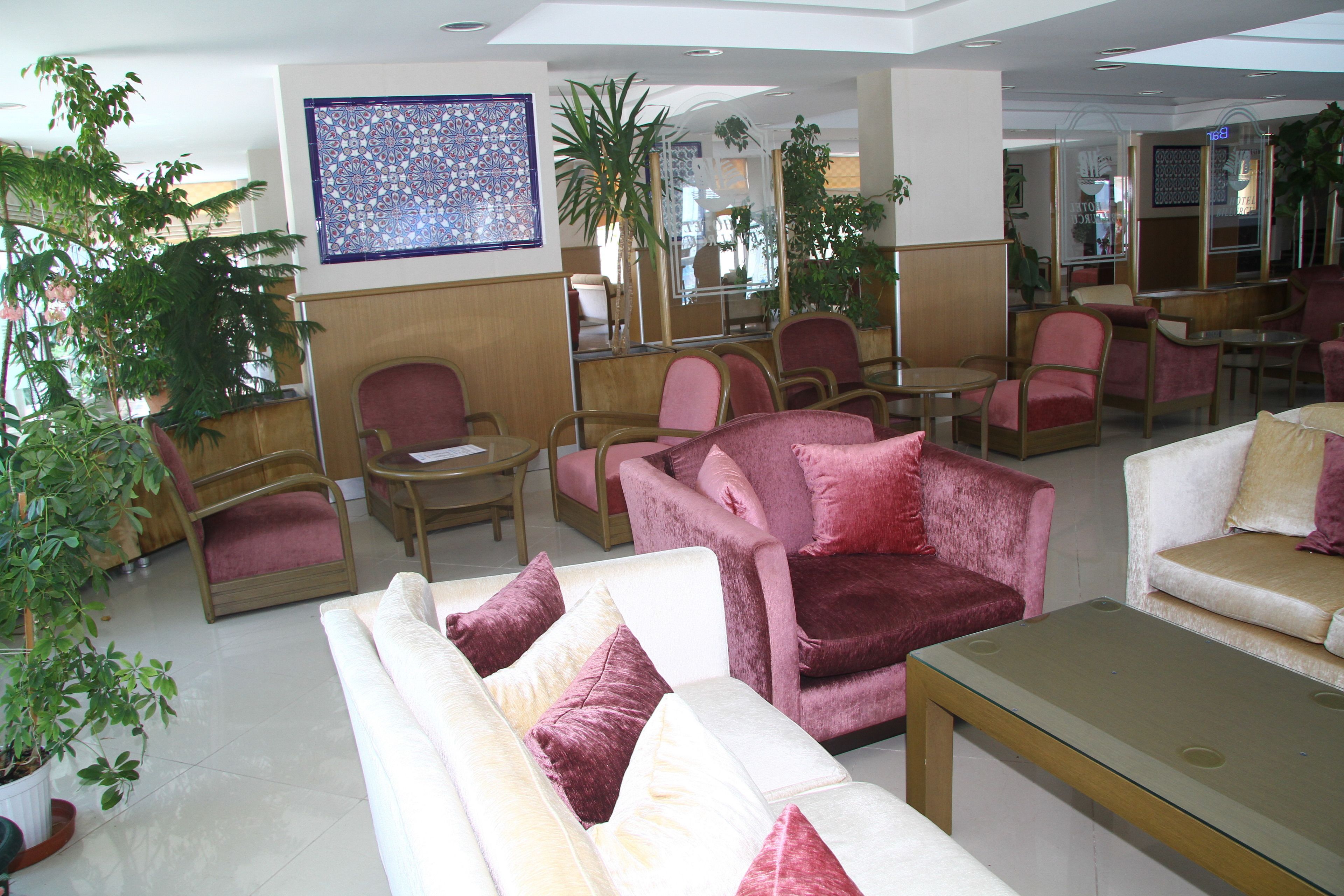 A hotel lobby with seating areas, a large decorative wall piece, and potted plants.