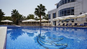 Una piscina con un mosaico de delfín, rodeada de sillas de descanso y sombrillas, y un edificio con amplias ventanas al fondo.