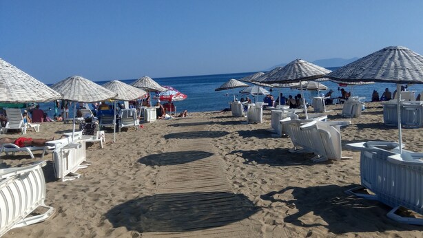 Una playa con filas de tumbonas y sombrillas, cielo despejado y el mar al fondo.