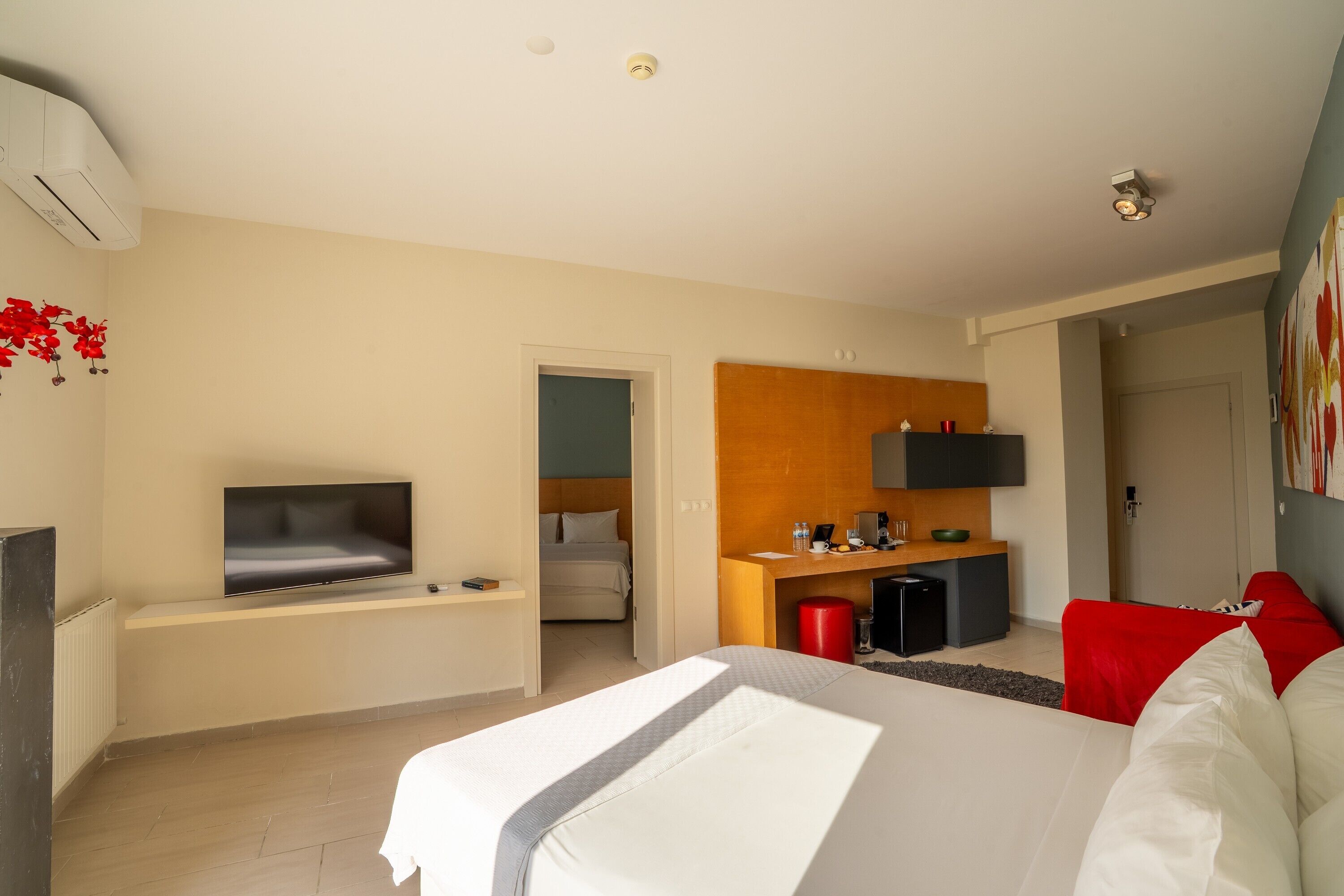 A hotel room with a bed, a TV, a desk with a computer, and a small kitchenette.