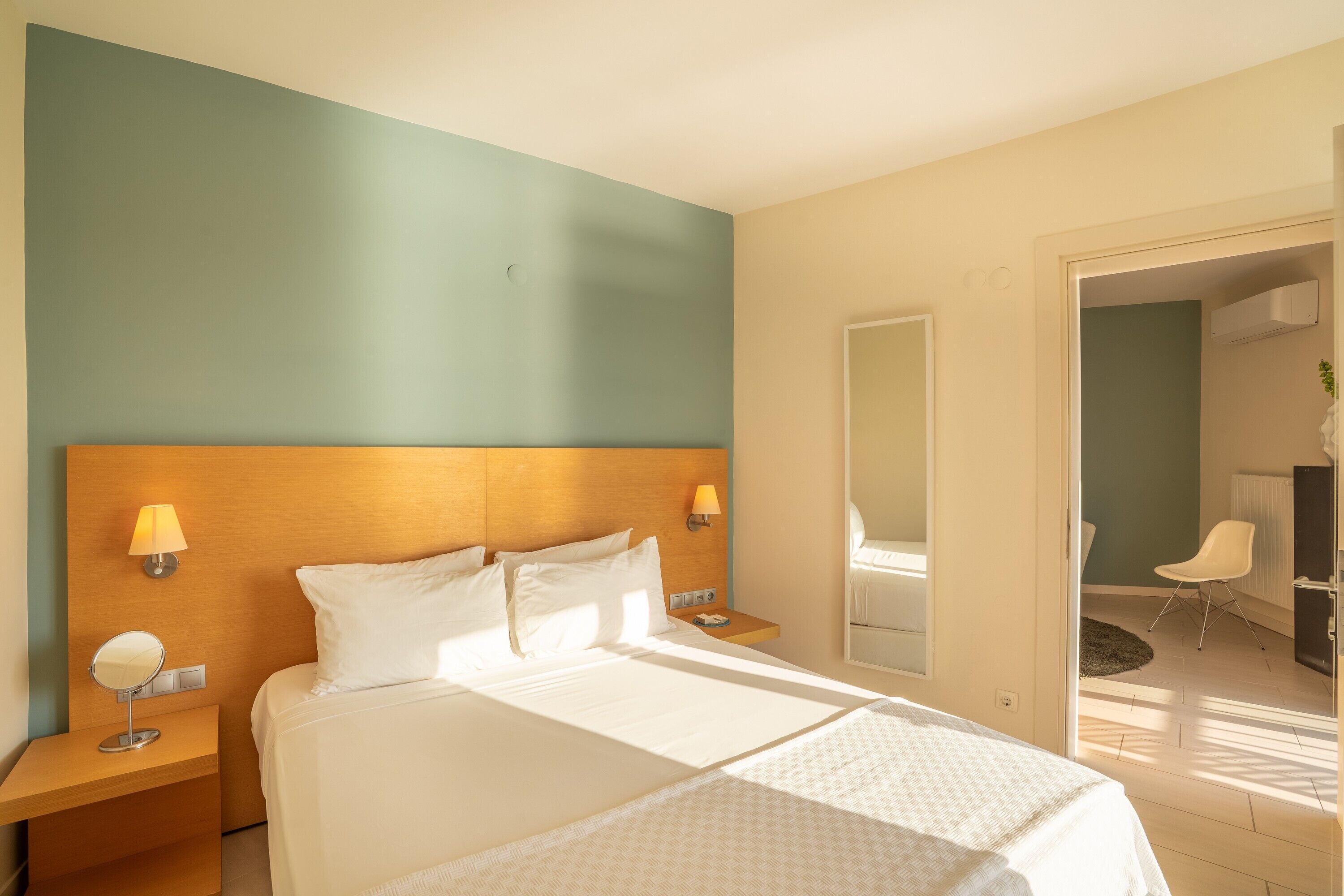 Une chambre d’hôtel avec un grand lit, deux tables de chevet, un miroir et une vue sur la salle de bain et le balcon.