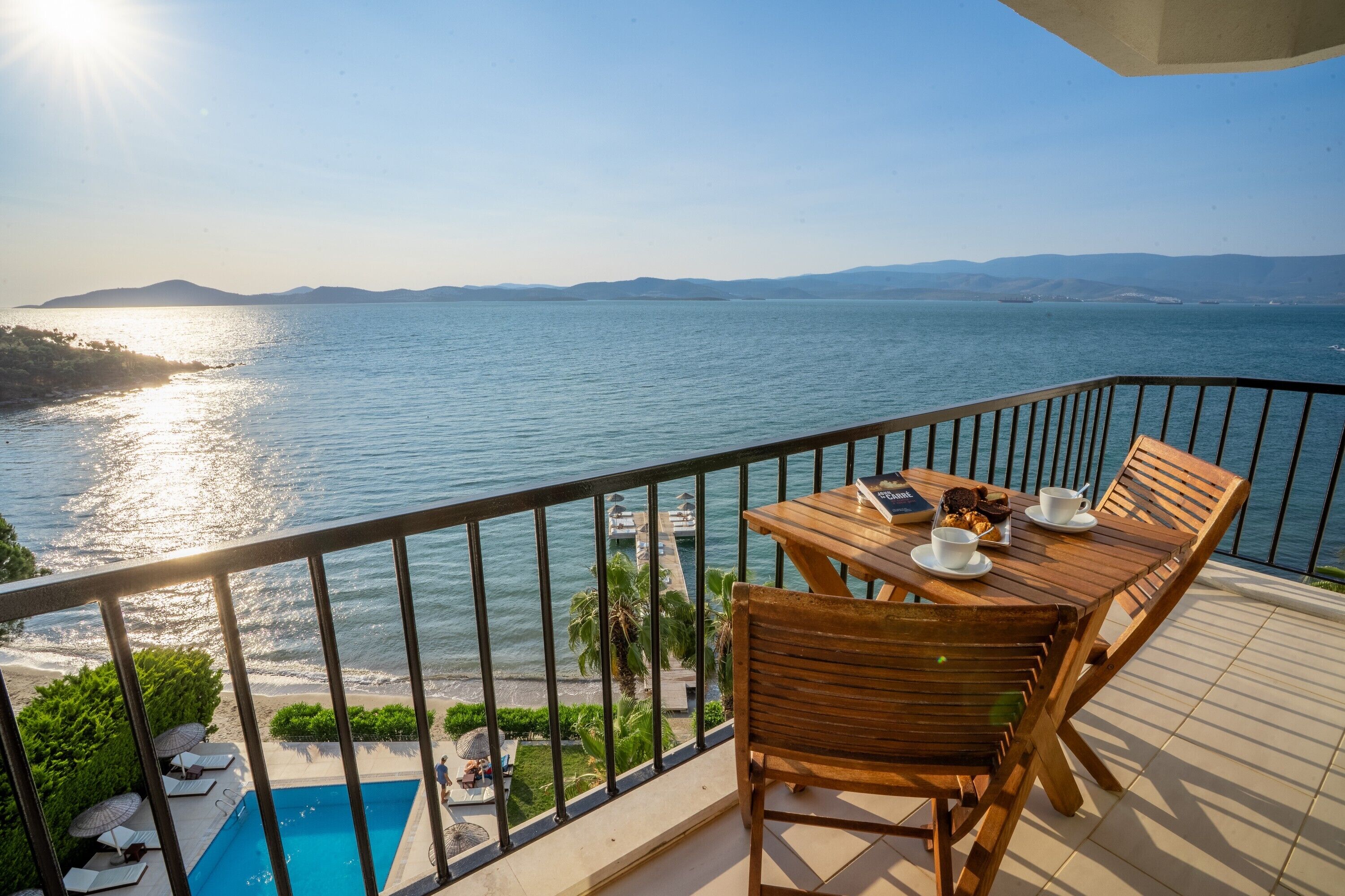 Un balcon avec une table et des chaises donnant sur une piscine et une plage.