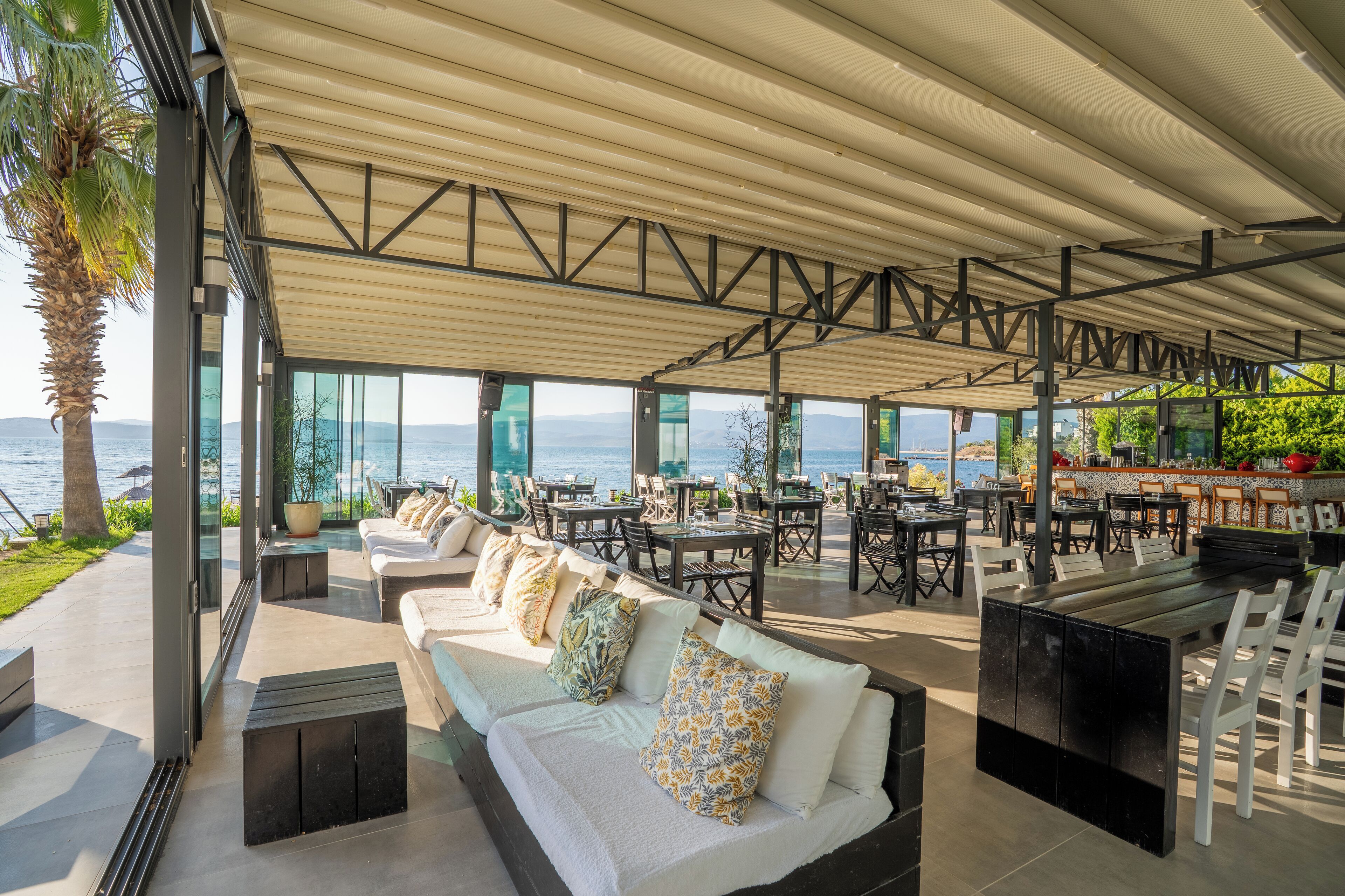 Un área de estar moderna al aire libre con vistas al mar, que incluye sofás, mesas y sillas.