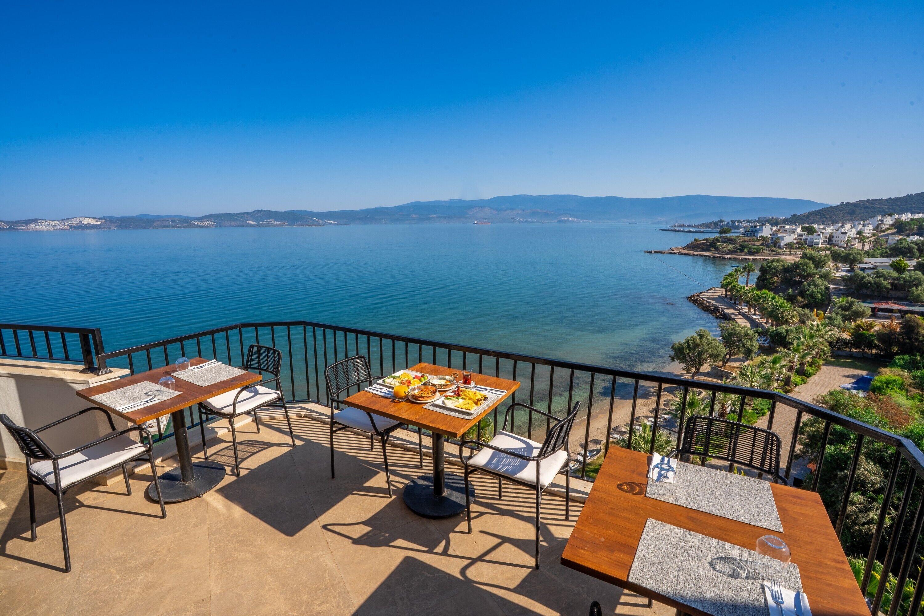 Una terraza con mesa y sillas de madera que da a un mar tranquilo.