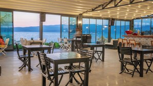 A restaurant with outdoor seating overlooking a body of water, featuring large windows and a modern interior design. - Med-Inn Hotel (Milas)