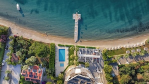 An aerial view of a coastal resort with a pier extending into the sea, a swimming pool, and a building with multiple balconies. - Med-Inn Hotel (Milas)