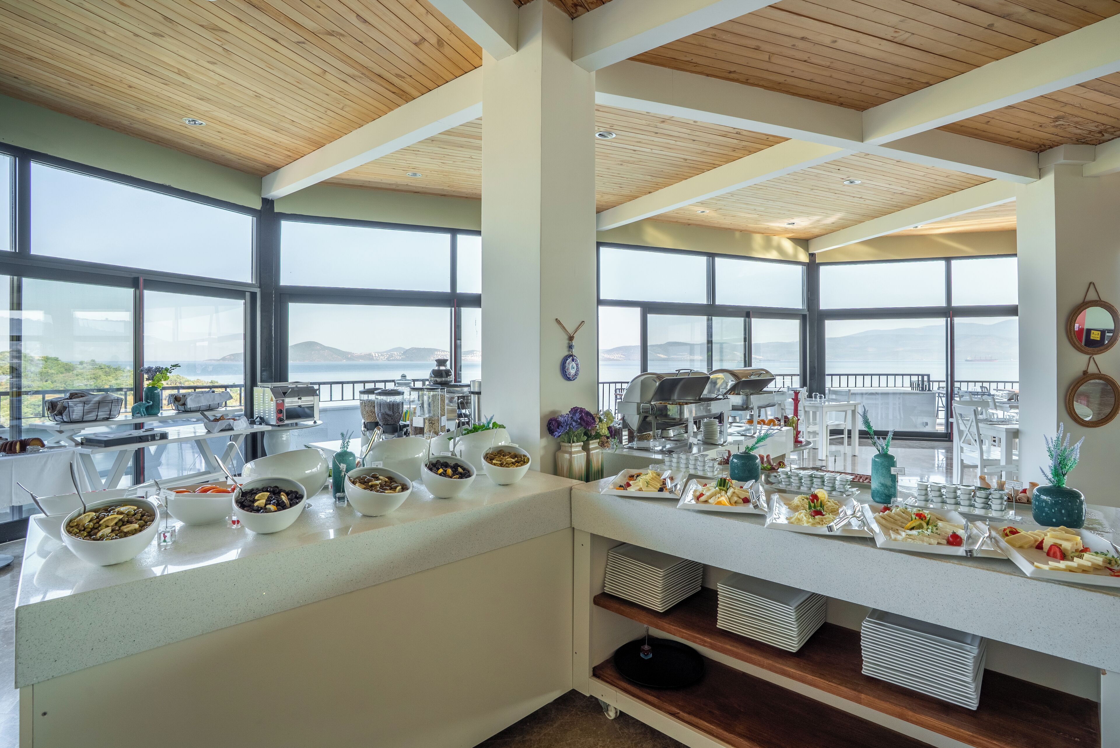 Montaje de bufé con diferentes alimentos y una estación de café, ventanas amplias con vistas a las montañas y techo de madera.