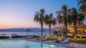 A poolside area with lounge chairs, umbrellas, and a view of the sea at dusk. - Med-Inn Hotel (Milas)