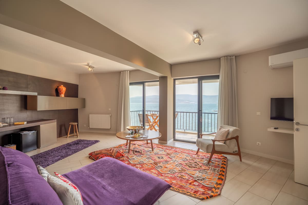 A modern living room with a sofa, a patterned rug, a dining table, and a view of the sea through large windows.