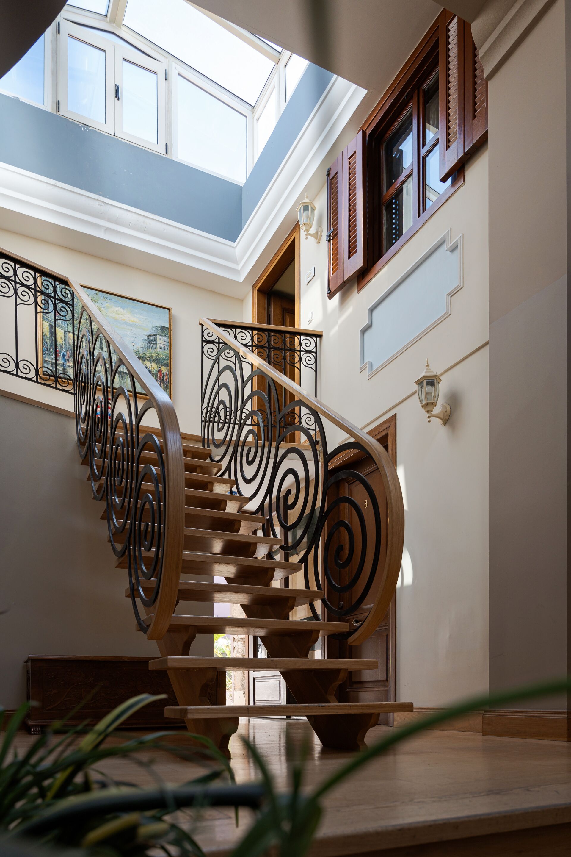 Una escalera de madera con barandillas negras que conduce a un segundo piso con tragaluz.