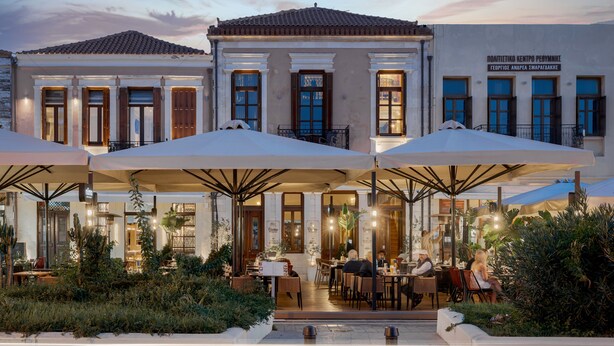 An outdoor cafe with tables and umbrellas, surrounded by greenery. - Civitas Suites Hotel (Rethymno)