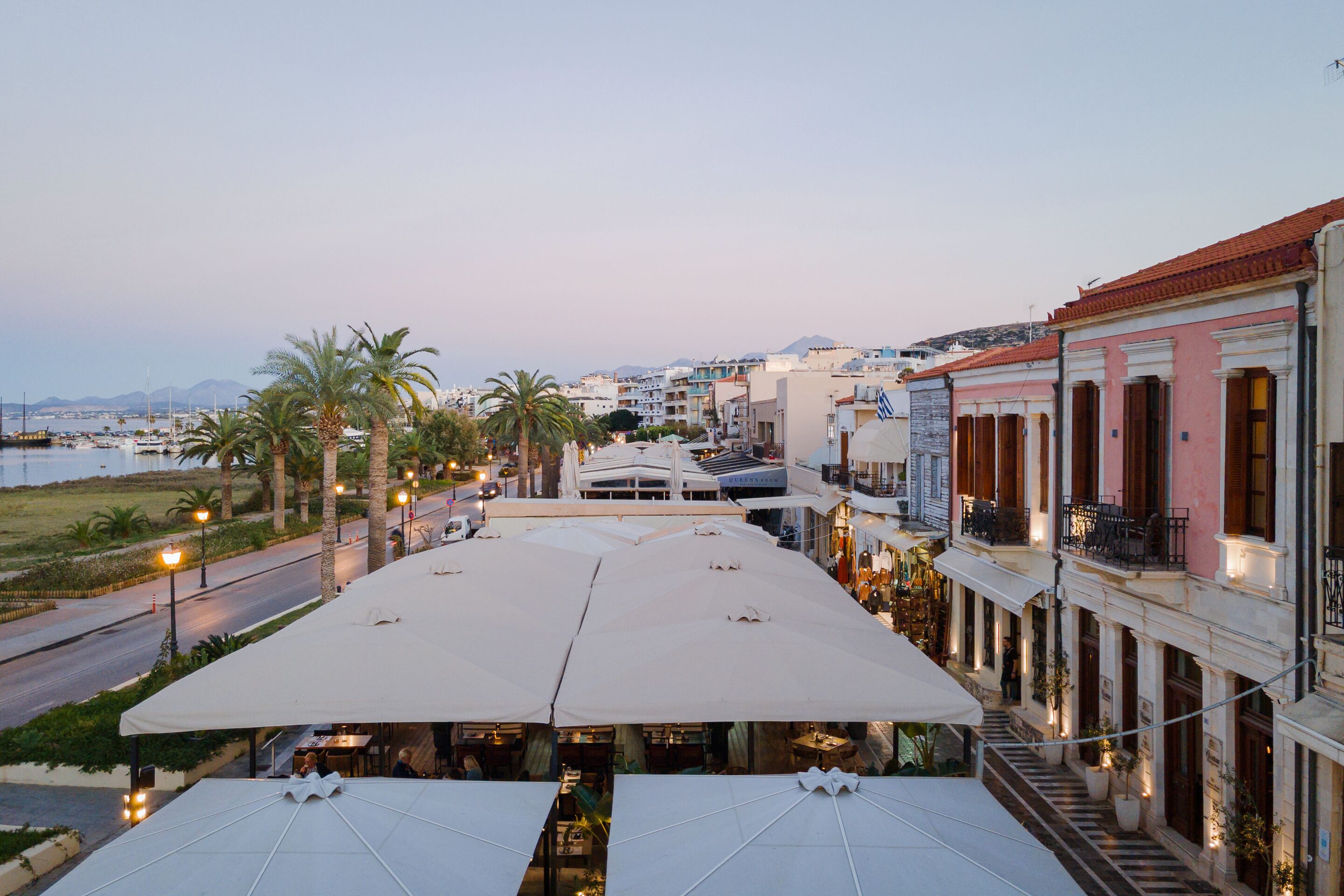 Un hotel frente al mar con terraza al aire libre y una calle bordeada de palmeras.