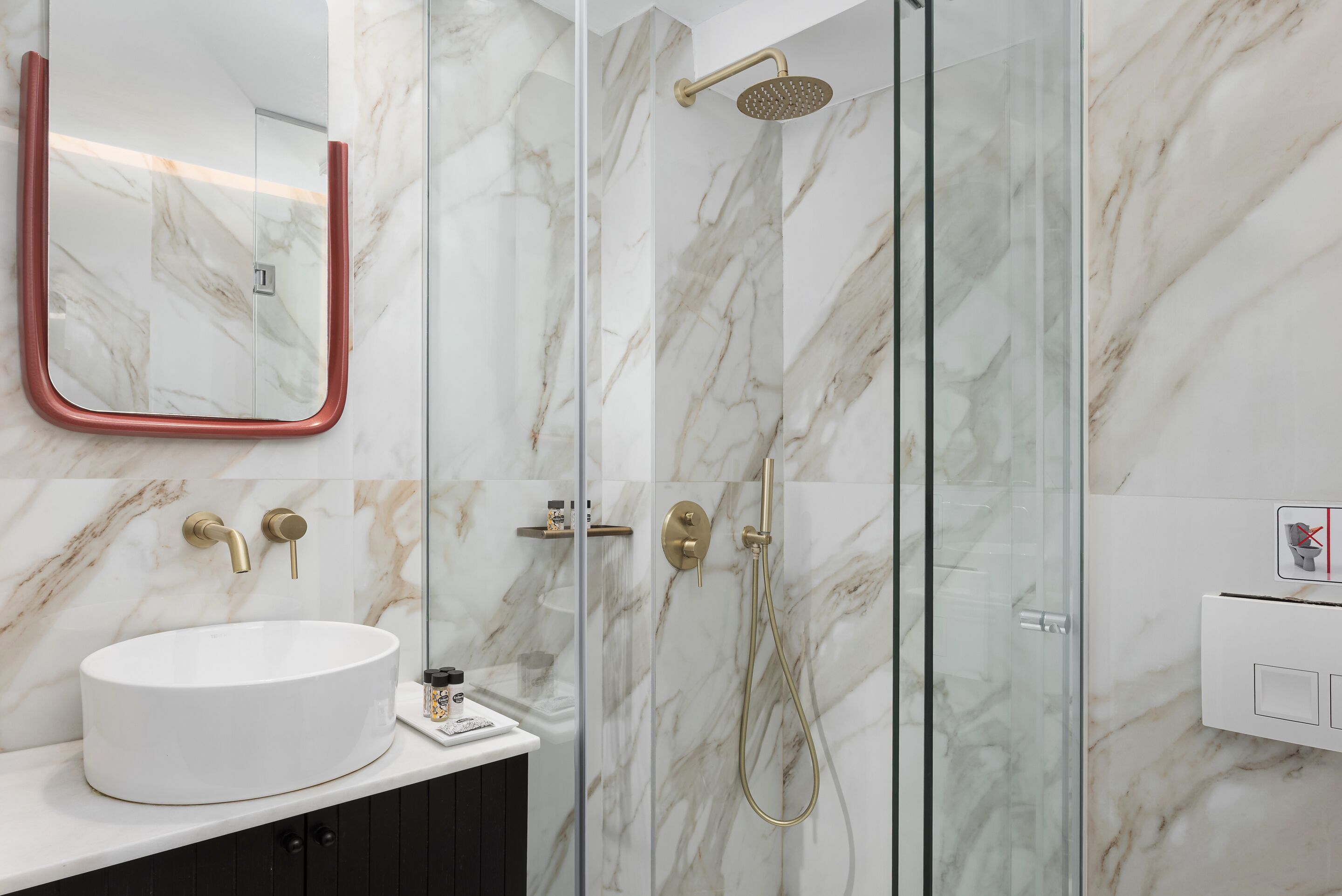 A modern bathroom with a marble shower enclosure, a white sink, and a glass door.