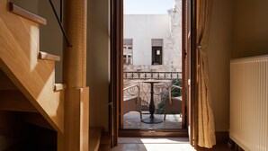 A room with a wooden staircase, a balcony with wicker chairs, and a view of a building outside. - Civitas Suites Hotel (Rethymno)