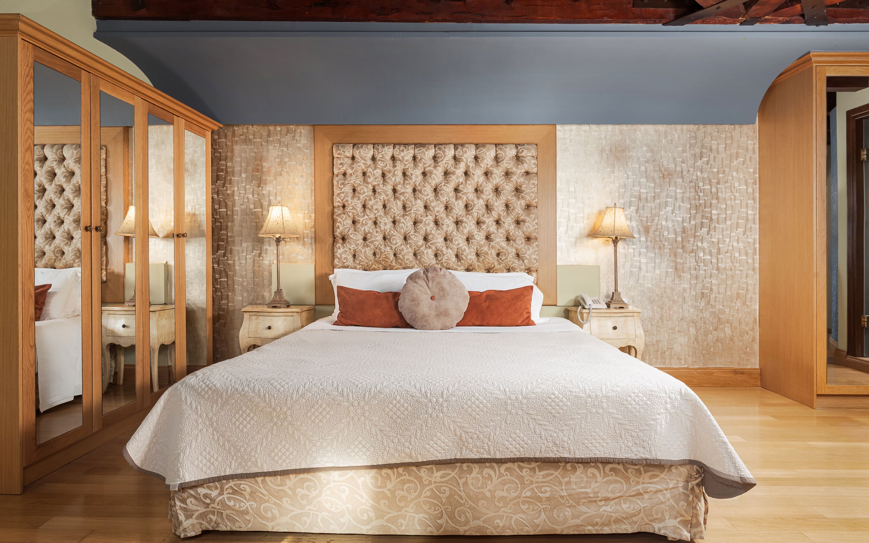 A spacious bedroom with a large bed, wooden wardrobe, and a decorative headboard.
