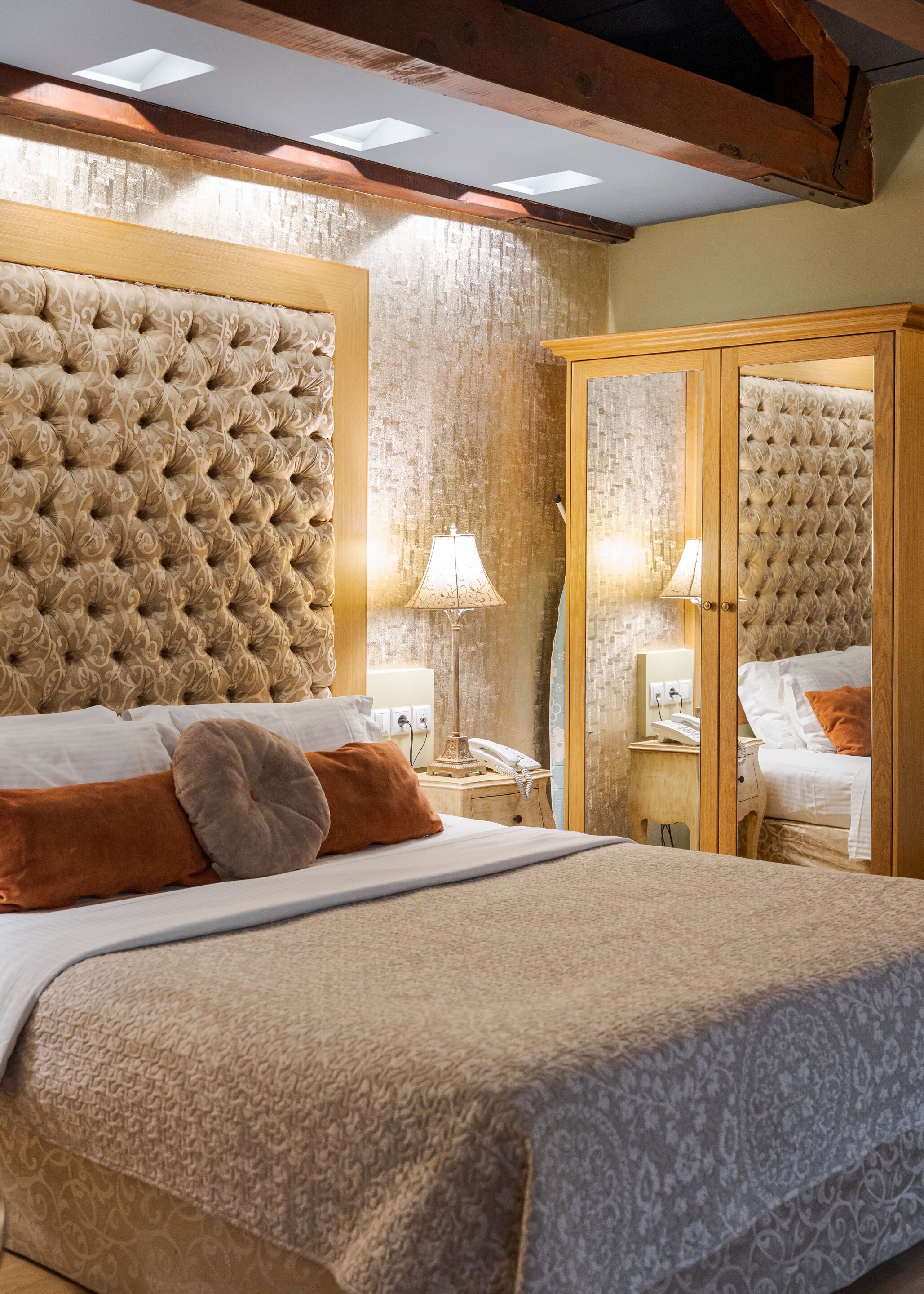 Une chambre d’hôtel dotée d’une grande tête de lit capitonnée, d’une armoire en bois, d’une table de chevet avec une lampe et d’un téléphone.
