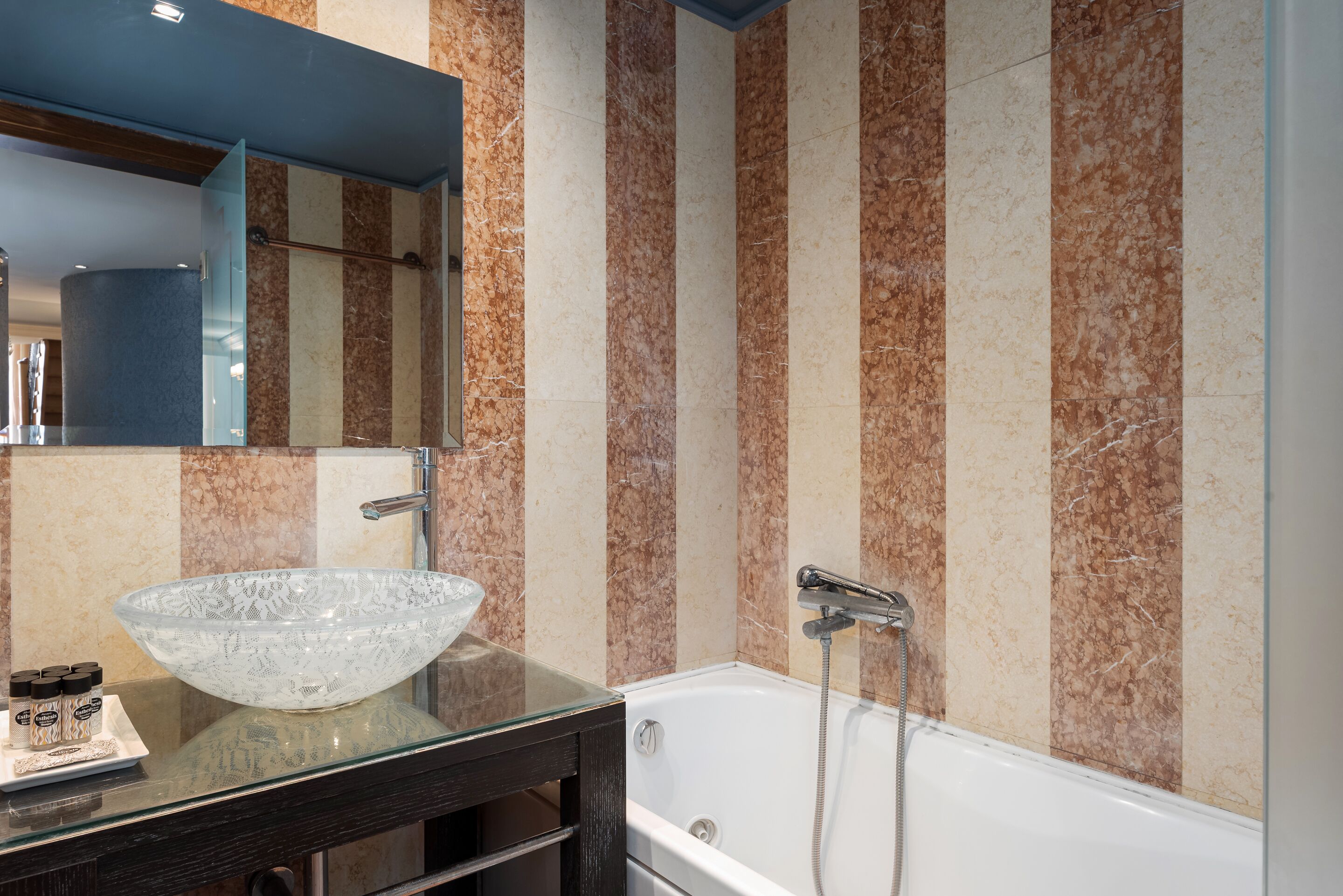 Ein Badezimmer mit einem Waschbecken aus Glas, einem großen Spiegel, einer Badewanne und Wänden mit marmorstreifen.