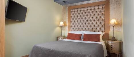 A bedroom with a bed, two bedside tables with lamps, a flat-screen TV mounted on the wall, and a decorative headboard.