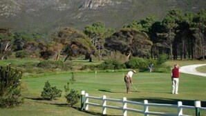 A golf course with a white fence, trees, and a mountain in the background. - Milkwood Lodge - Hermanus (Hermanus)