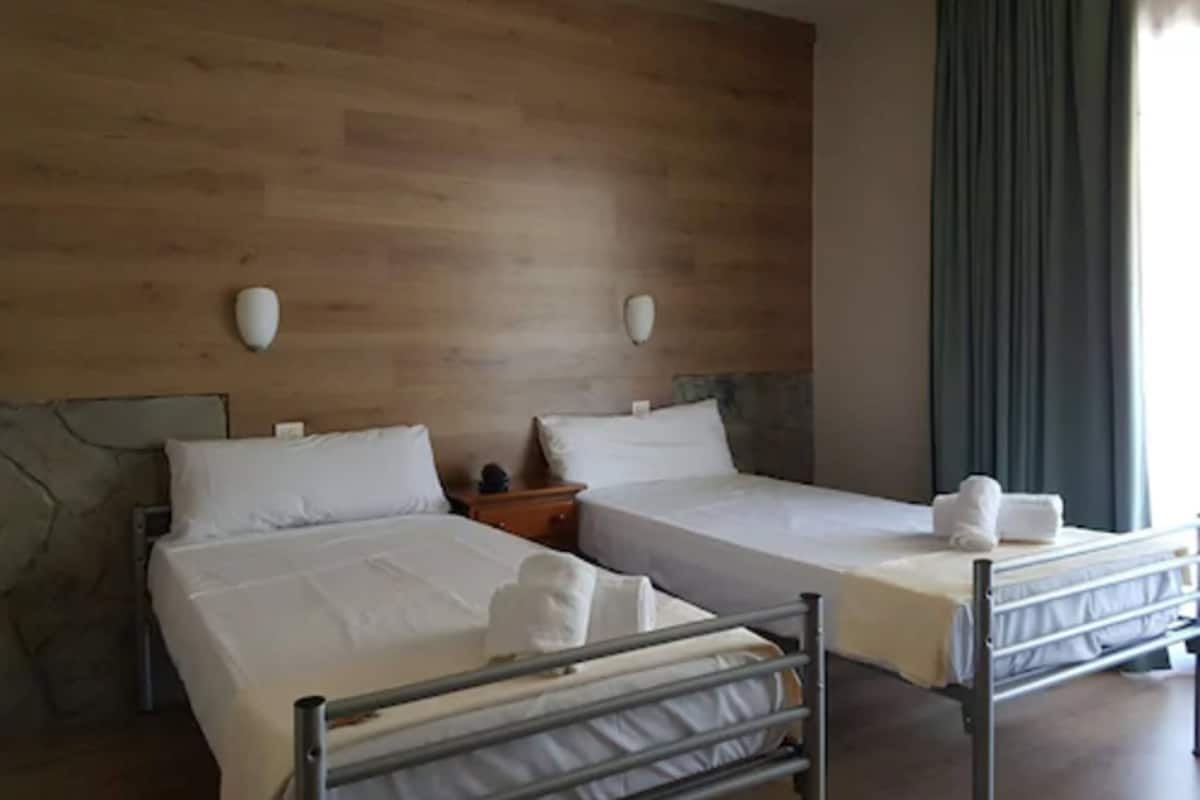 Habitación de hotel con dos camas, paneles de madera en las paredes y un ventanal con cortinas.