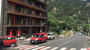 Een hotel met meerdere verdiepingen, balkons, een verharde weg en een bergachtige achtergrond.