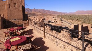 Une terrasse avec des tables et des chaises, une vue sur un paysage désertique et un bâtiment traditionnel doté d’une tour.