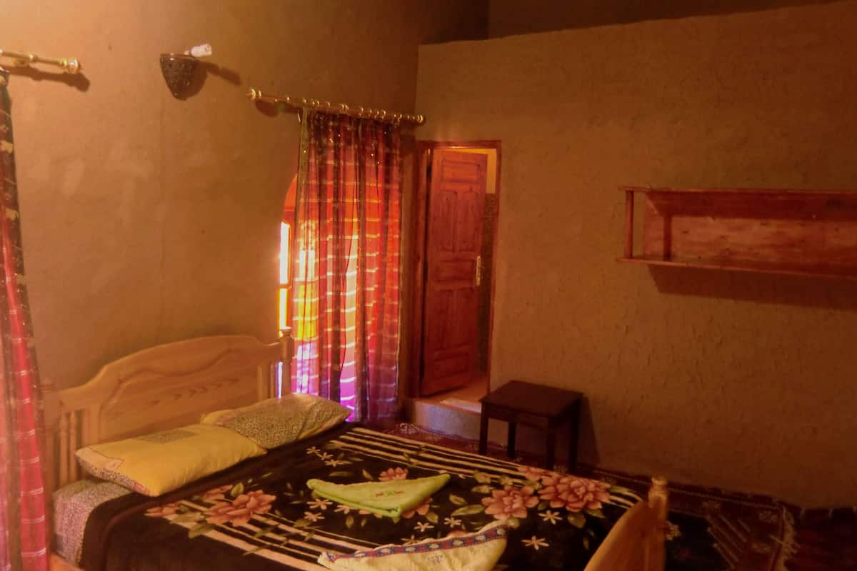 Une chambre à coucher avec un lit, une table de chevet, une petite table et une fenêtre avec des rideaux.